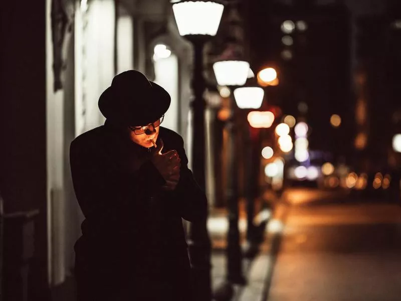 man with hat lighting cigarette on city street