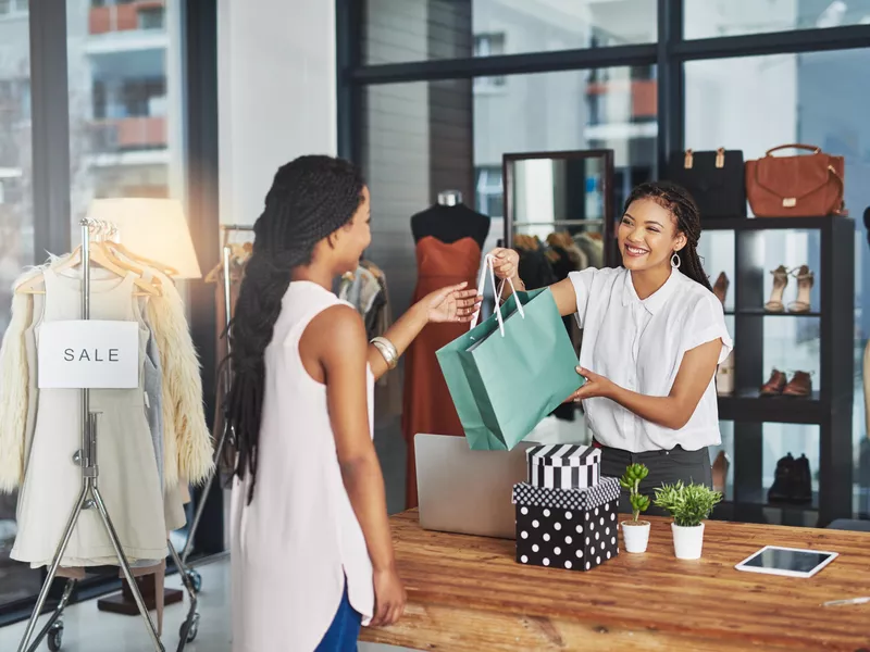 Young store owner handing a bag of paid goods to a customer