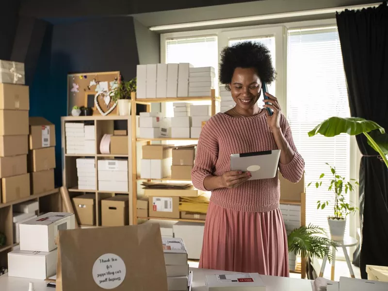 Smiling female business owner using digital tablet and talking on the phone