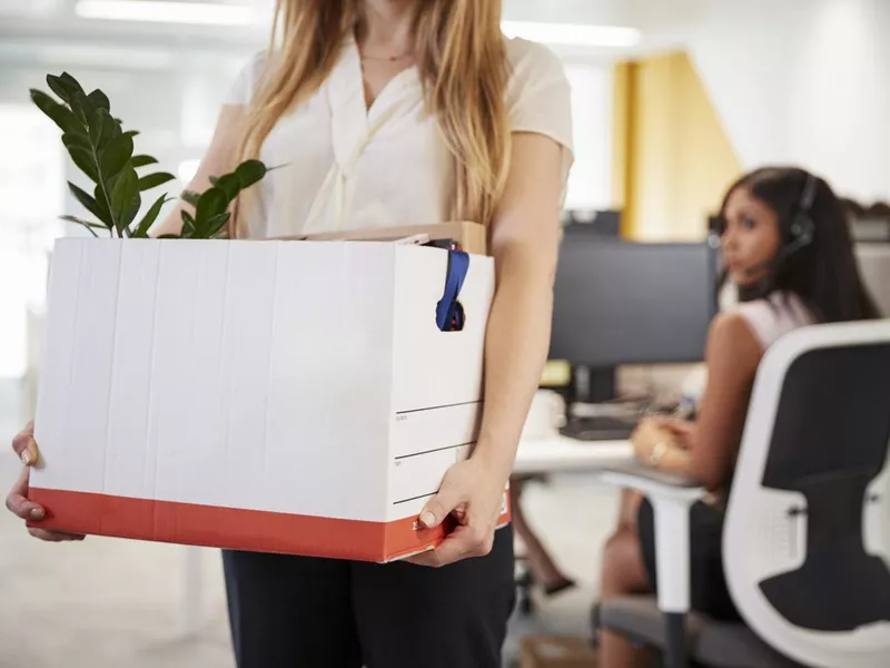 Fired female employee holding box of belongings in an office