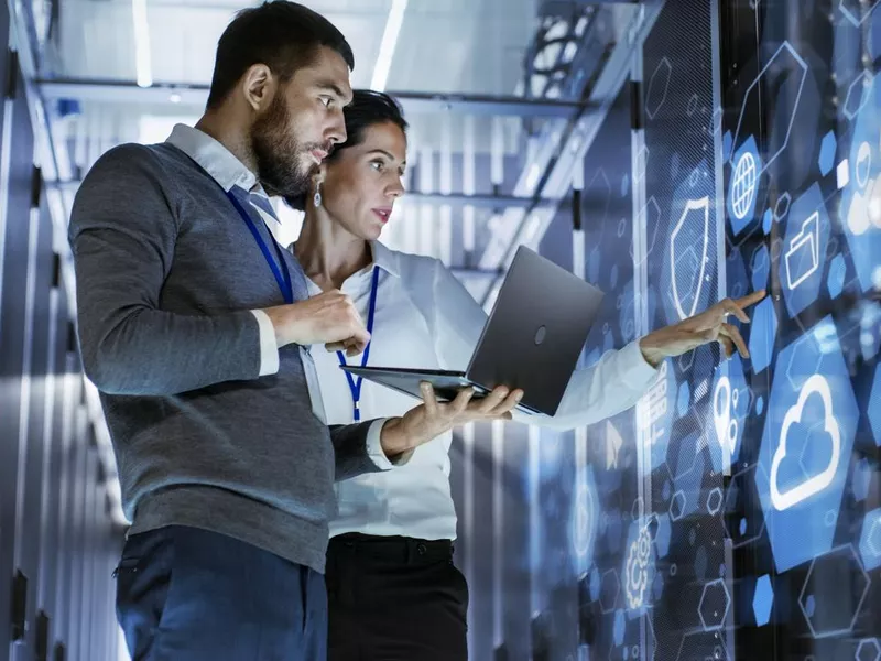 Male IT specialist holding laptop and discussing work with female server technician in data center