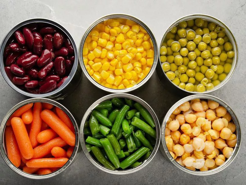 Canned carrots, chickpeas, kidney beans, green beans, peas and corn in opened tin cans on kitchen table. Non-perishable foods background