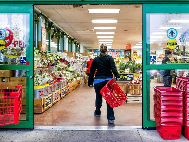 Trader Joe's customer trolley shopping basket carrying carts by store entrance doors outside women, winter flower pots, gardening plants, pineapple in Virginia