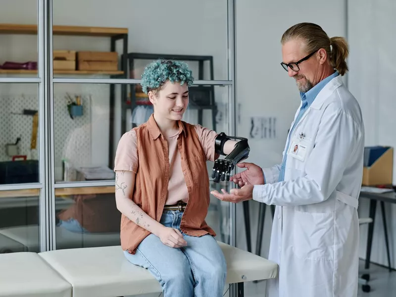 Smiling young woman with prosthetic arm consulting doctor