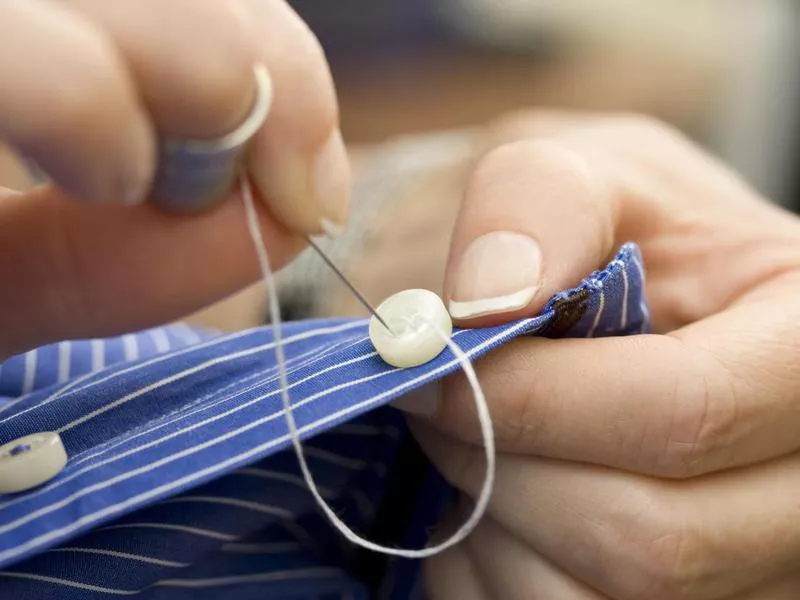 Close-up of a person sewing on white button on striped shirt