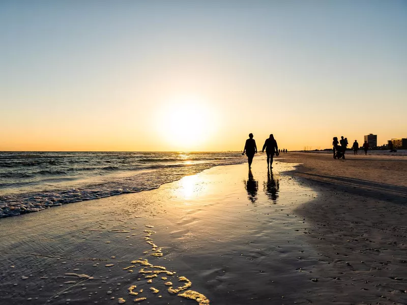 Sarasota, USA Sunset sun in Siesta Key, Florida with coastline ocean gulf of mexico on beach shore and many people couple silhouette walking by waves