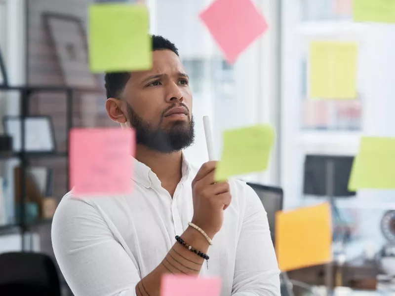 Shot of a young businessman brainstorming with sticky notes on a glass wall in an office