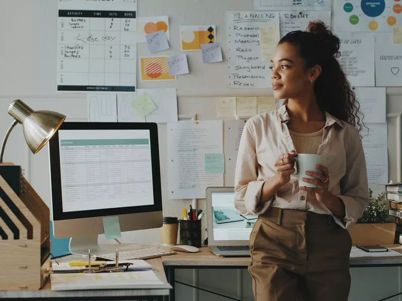 Shot of an attractive young businesswoman standing and looking contemplative while holding a cup of coffee in her home office