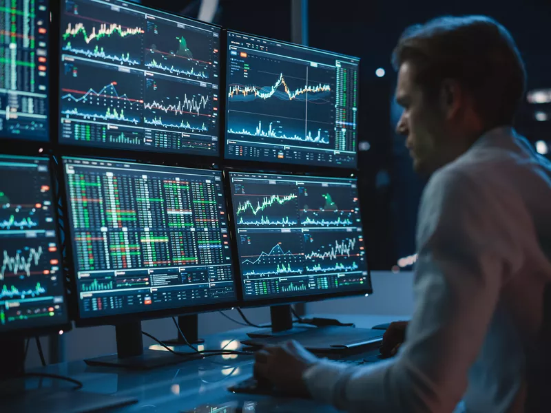 Financial analyst working on a computer with many monitors