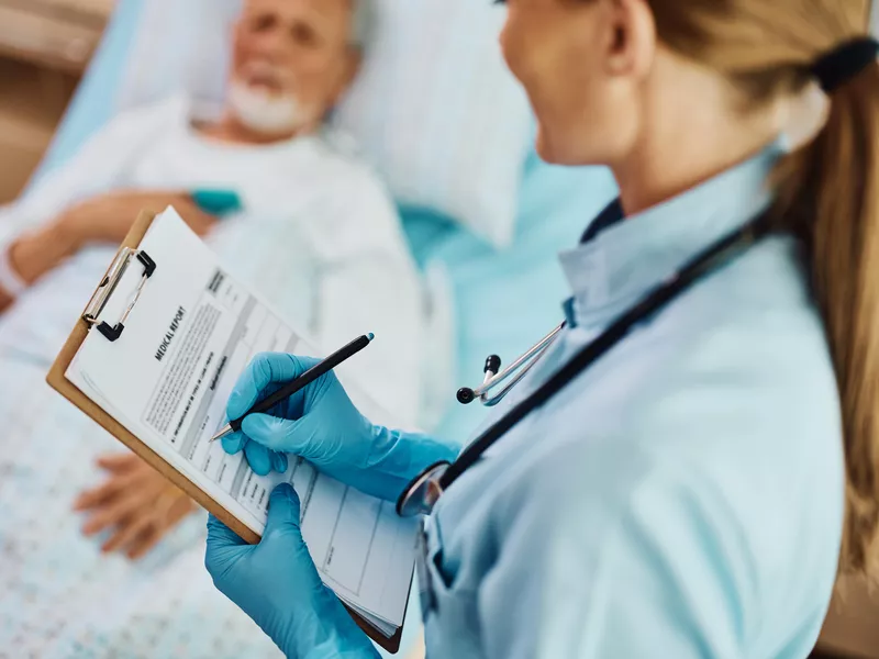 Nurse writing data in medical report while visiting patient at intensive care unit at hospital